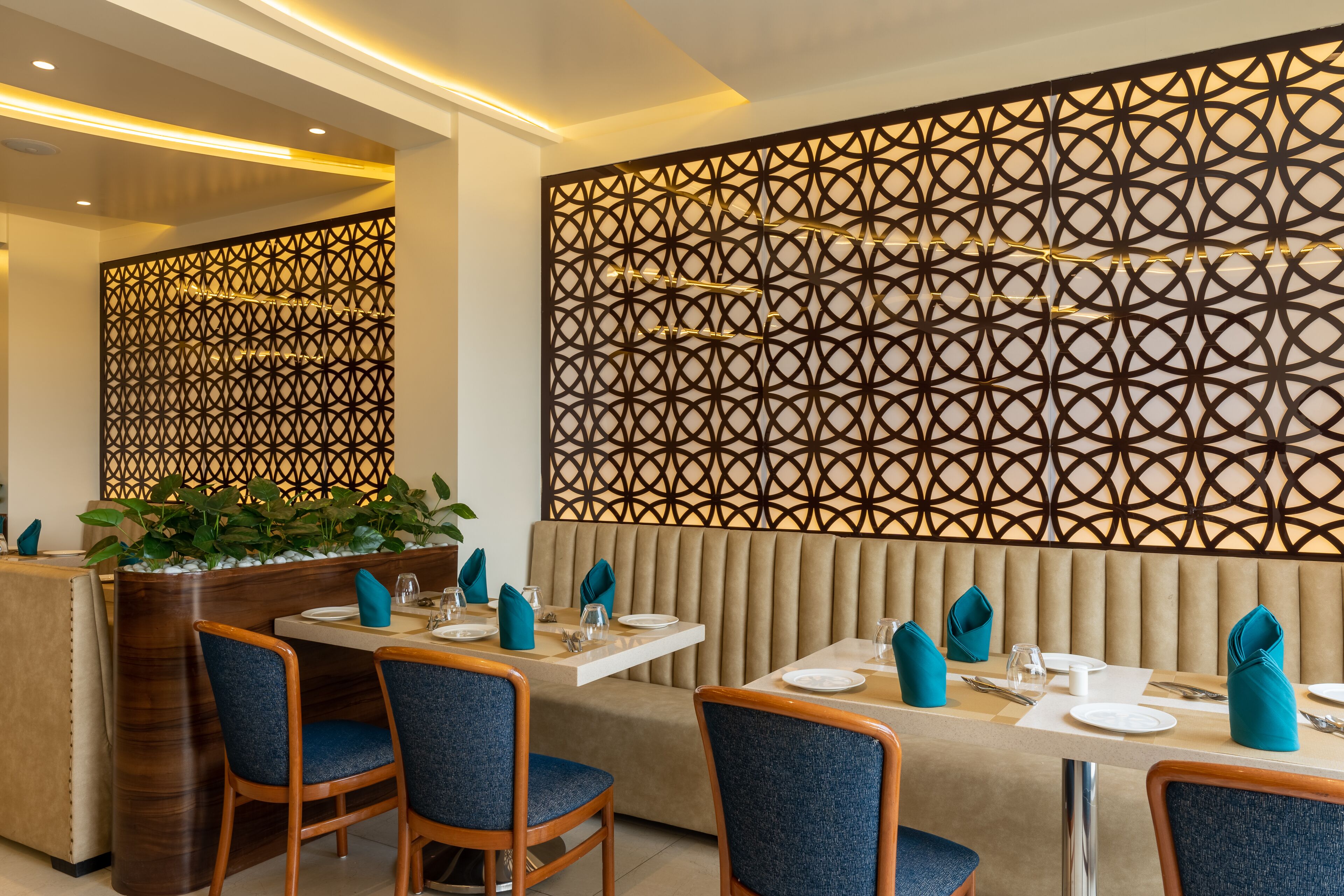 A restaurant with a modern interior, featuring a geometric patterned wall, cushioned seating, and neatly arranged tables with blue napkins.