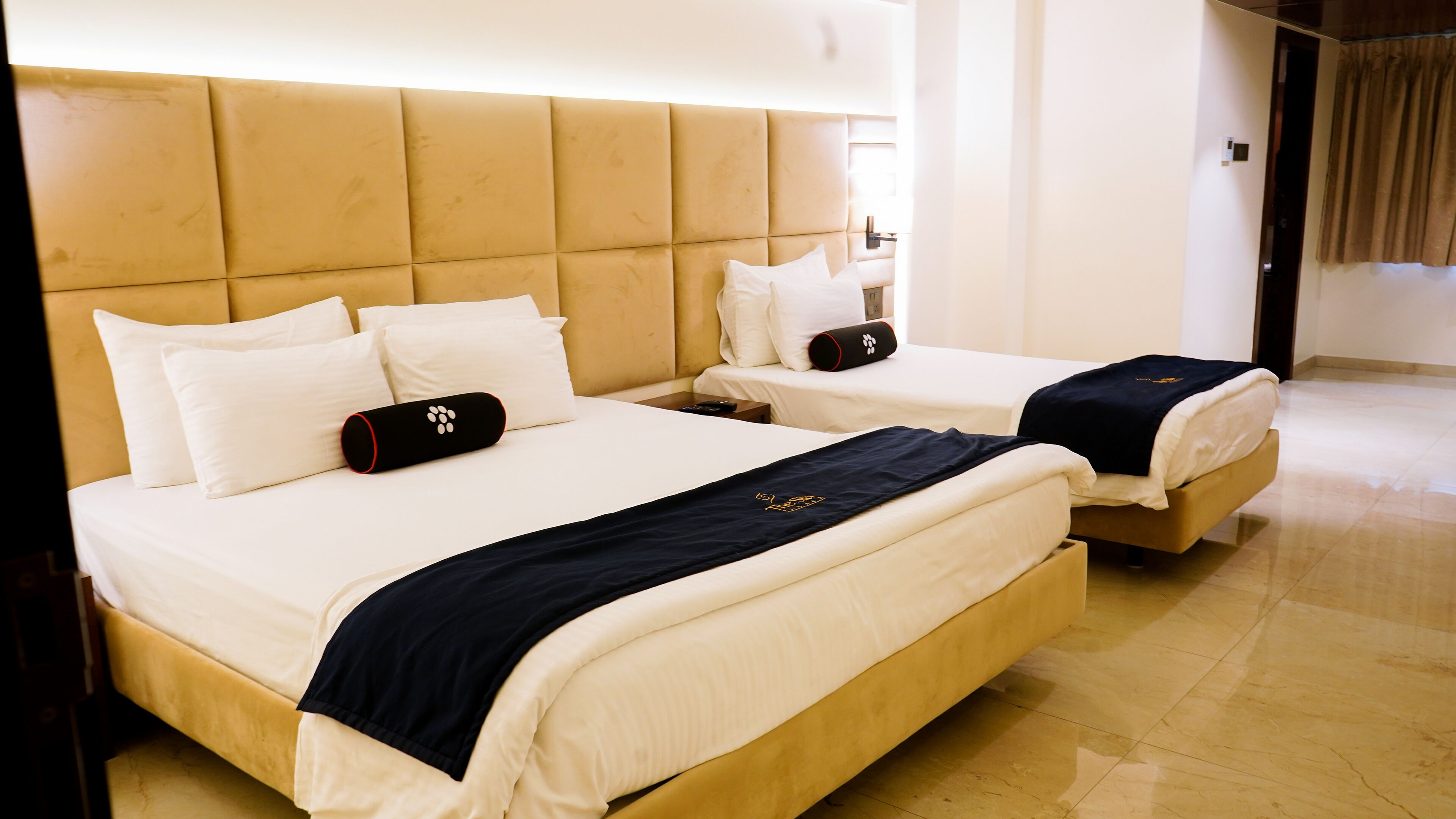 Hotellihuone, jossa on kaksi sänkyä, ja molemmissa on valkoiset vuodevaatteet sekä tummansininen peitto.