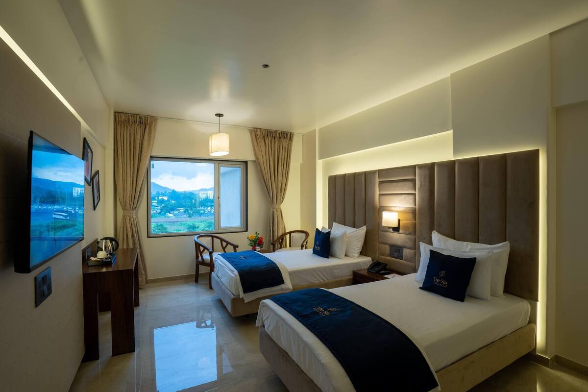 A hotel room with two beds, a desk, a TV, and a large window with a view.