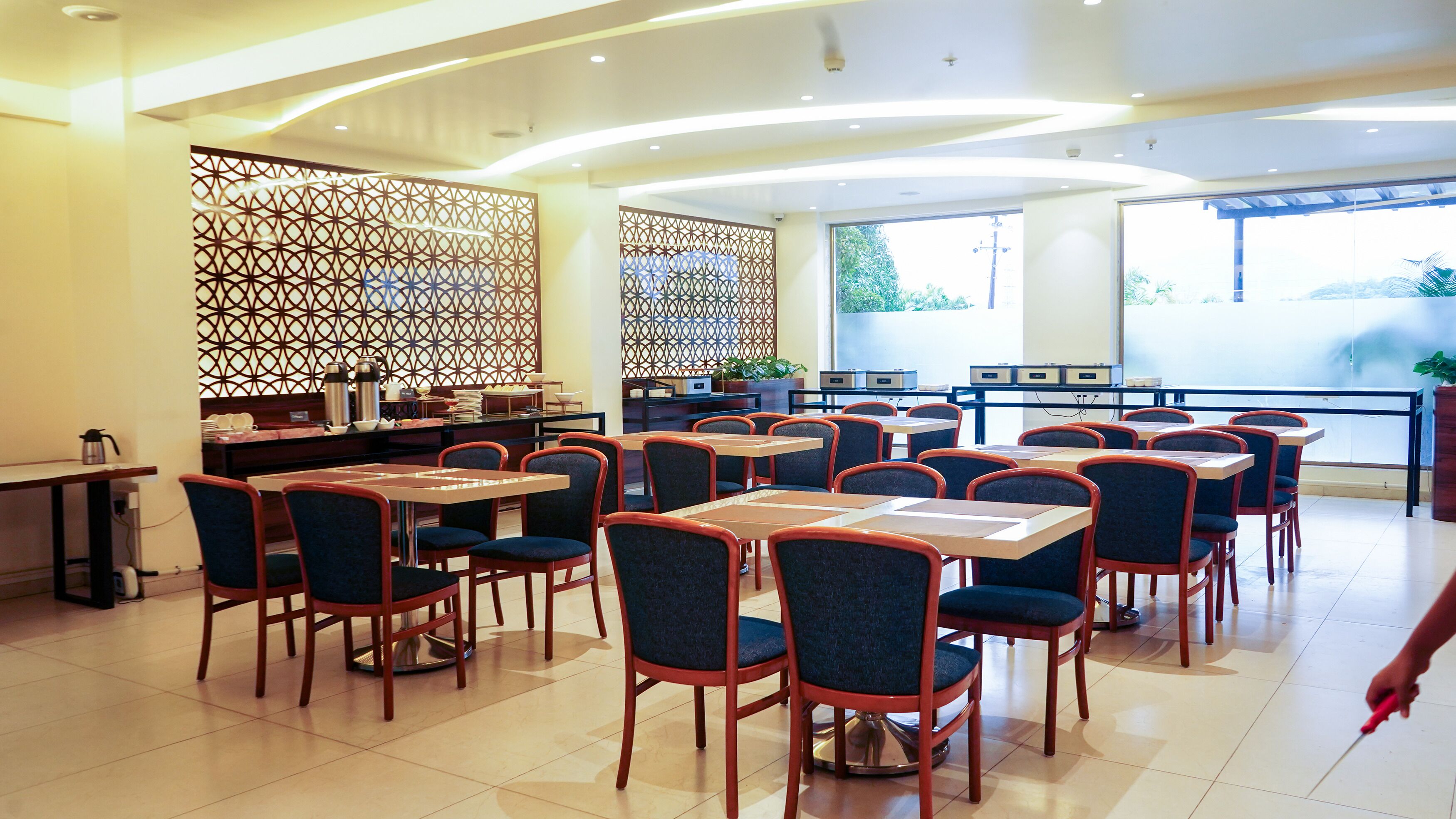 A spacious dining area with multiple tables and chairs, a decorative partition, and a view of the outdoors.