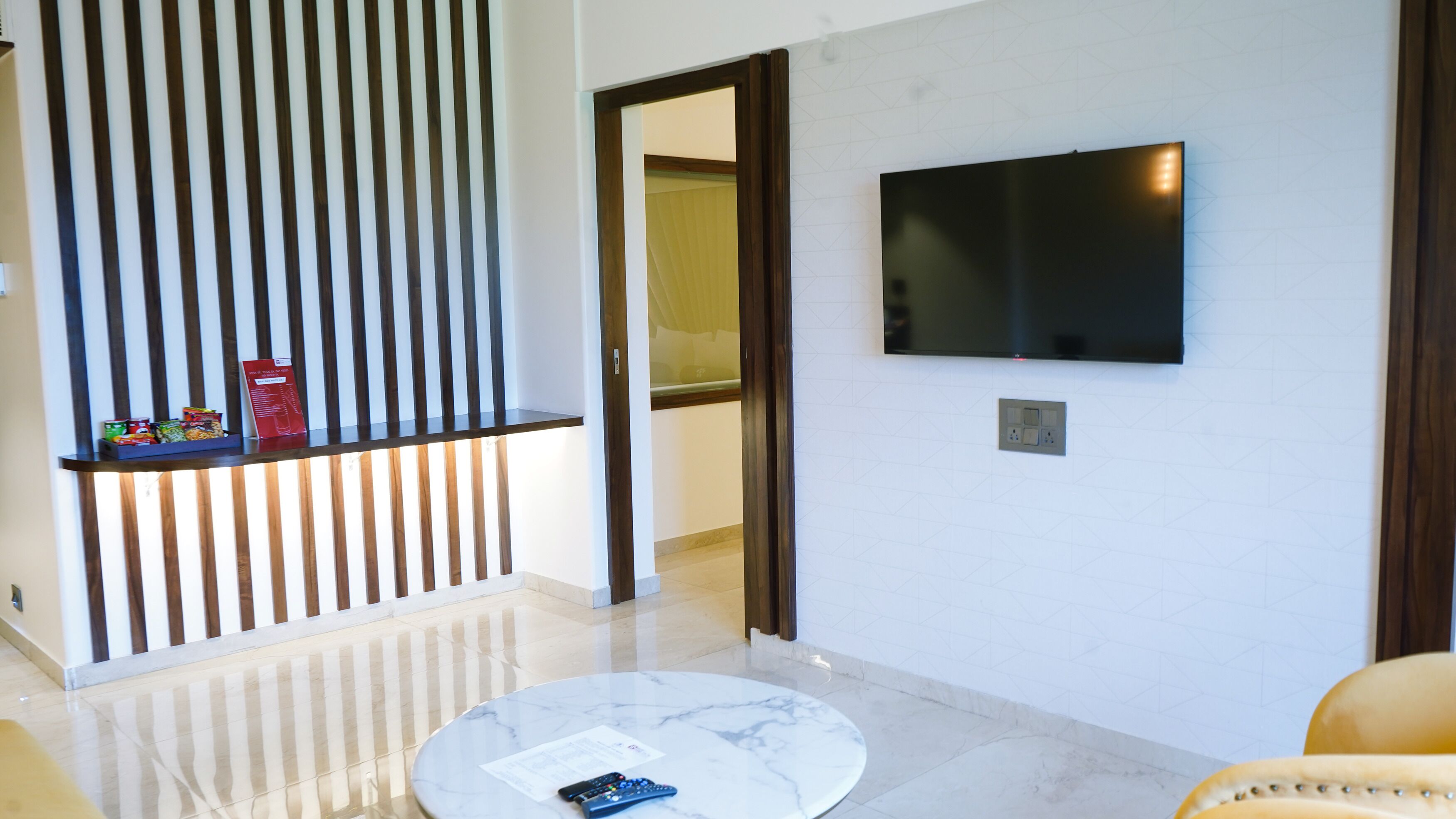 Un salon moderne avec une table basse en marbre, un téléviseur à écran plat fixé au mur et un paravent en bois à lattes.