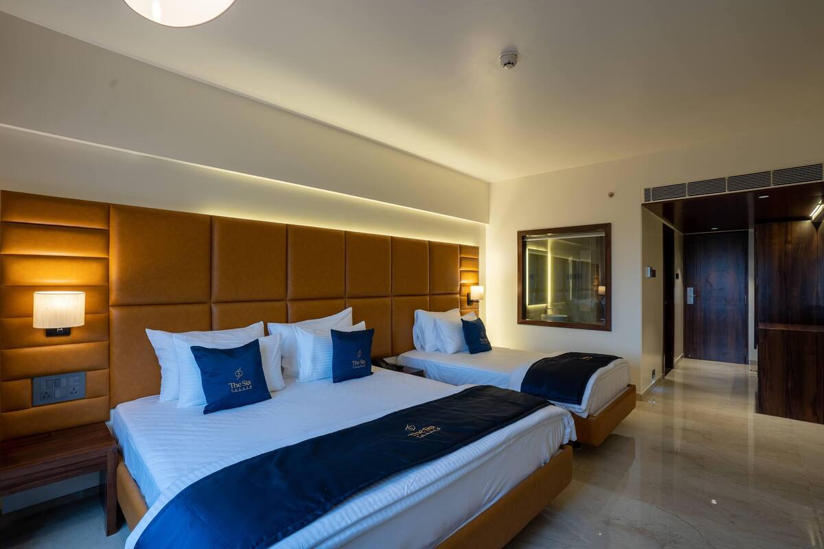 A hotel room with two beds, a large padded headboard, bedside lamps, and a mirror.