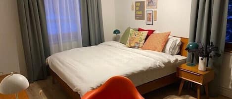 Una habitación de hotel con cama, escritorio, silla, mesita de noche y ventana con cortinas.