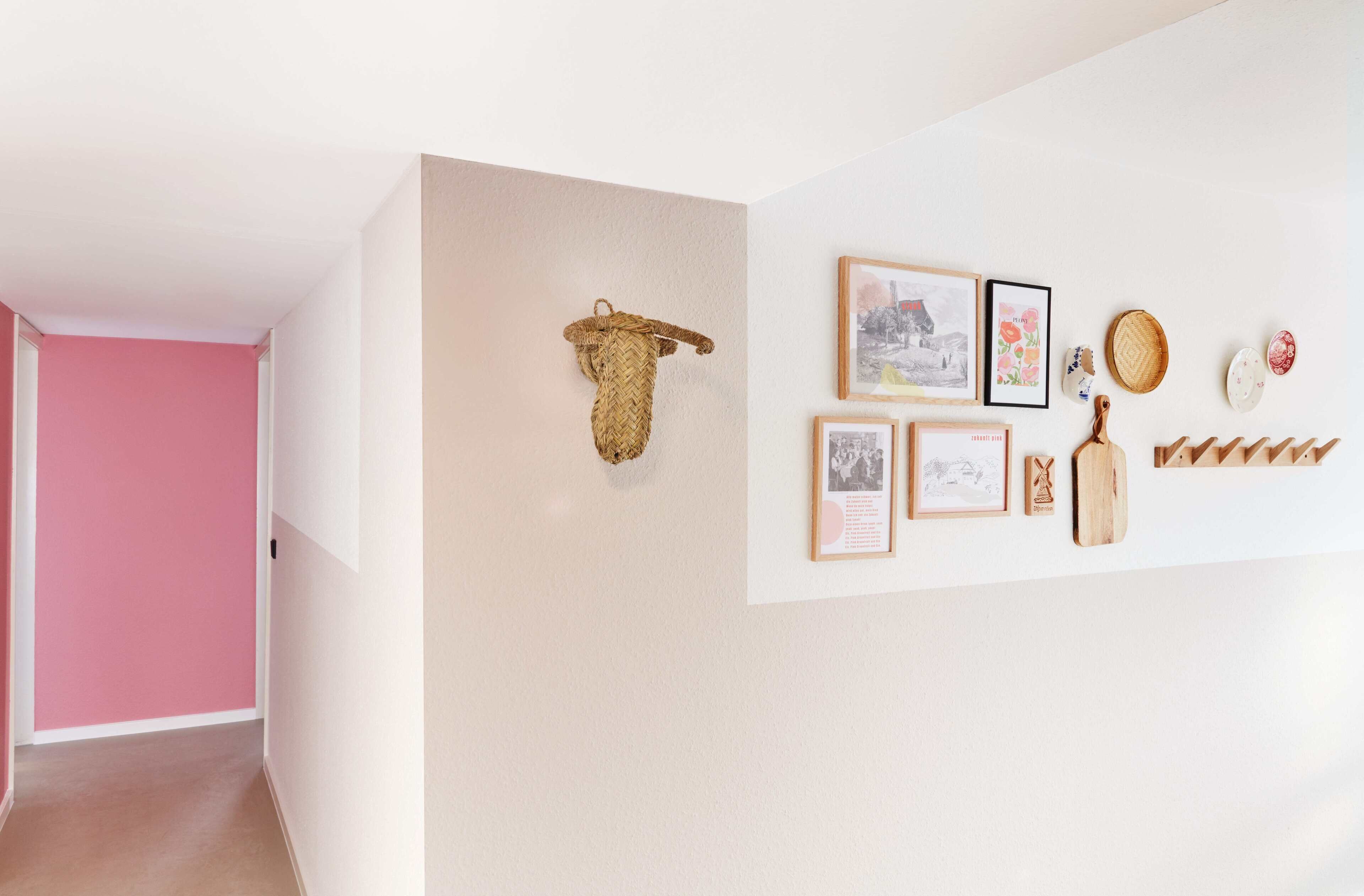 A hallway with a pink wall and a beige wall with wall art and a woven basket.