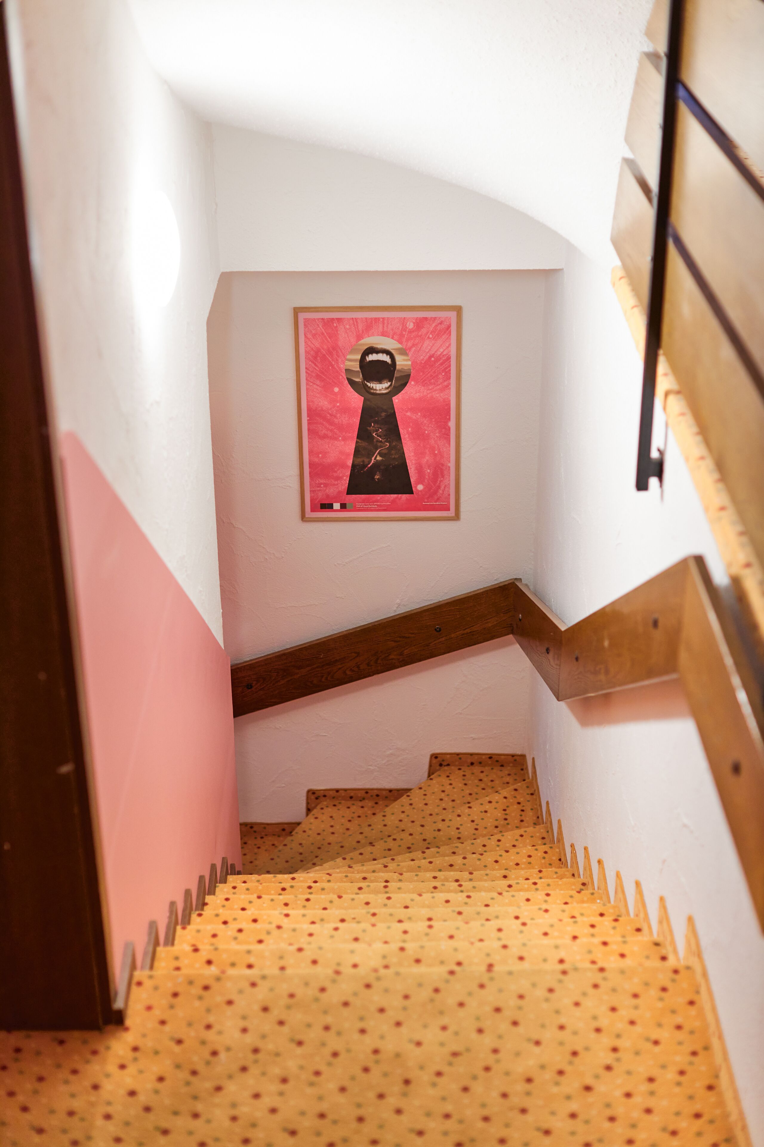 Een trap met een houten leuning en een roze muur met een ingelijste foto.