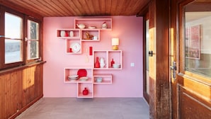 A room with wooden walls and ceiling, pink shelving units with various dishes and a lamp, and a wooden door with a glass panel. - pop-up stuub bierhäusle feldberg (Feldberg)