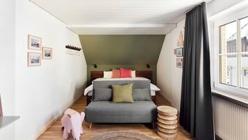 A narrow room with a bed, a small sofa, a wooden stool, and a window with curtains.