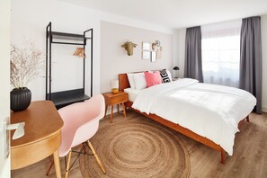 Un dormitorio moderno con una cama de madera, un escritorio con una silla, un tapete redondo y un espejo montado en la pared.