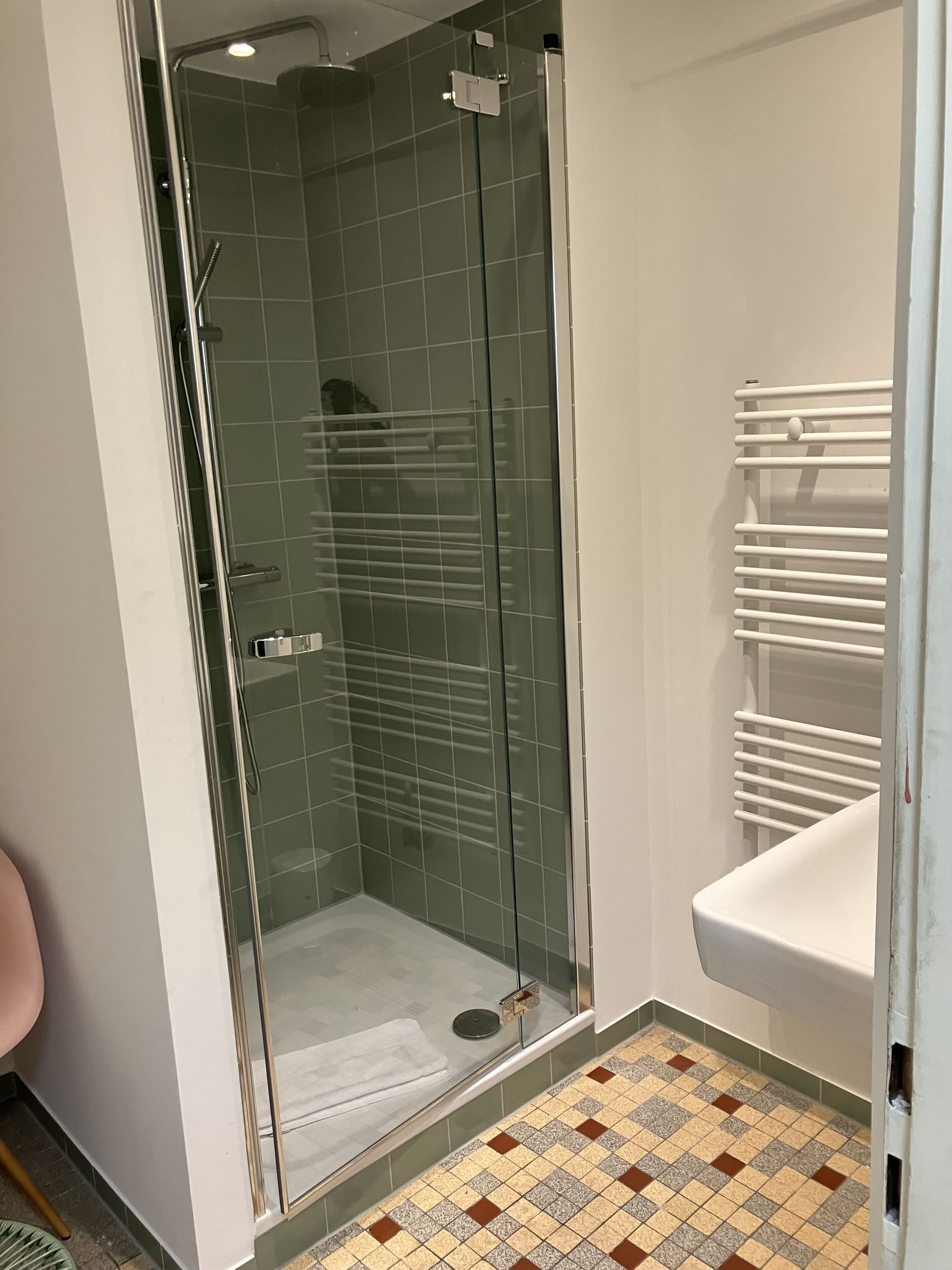 A glass-enclosed shower with a tiled floor, a white sink, and a towel rack.