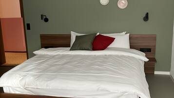 A neatly made bed with white bedding in a room with green walls and a wooden headboard.