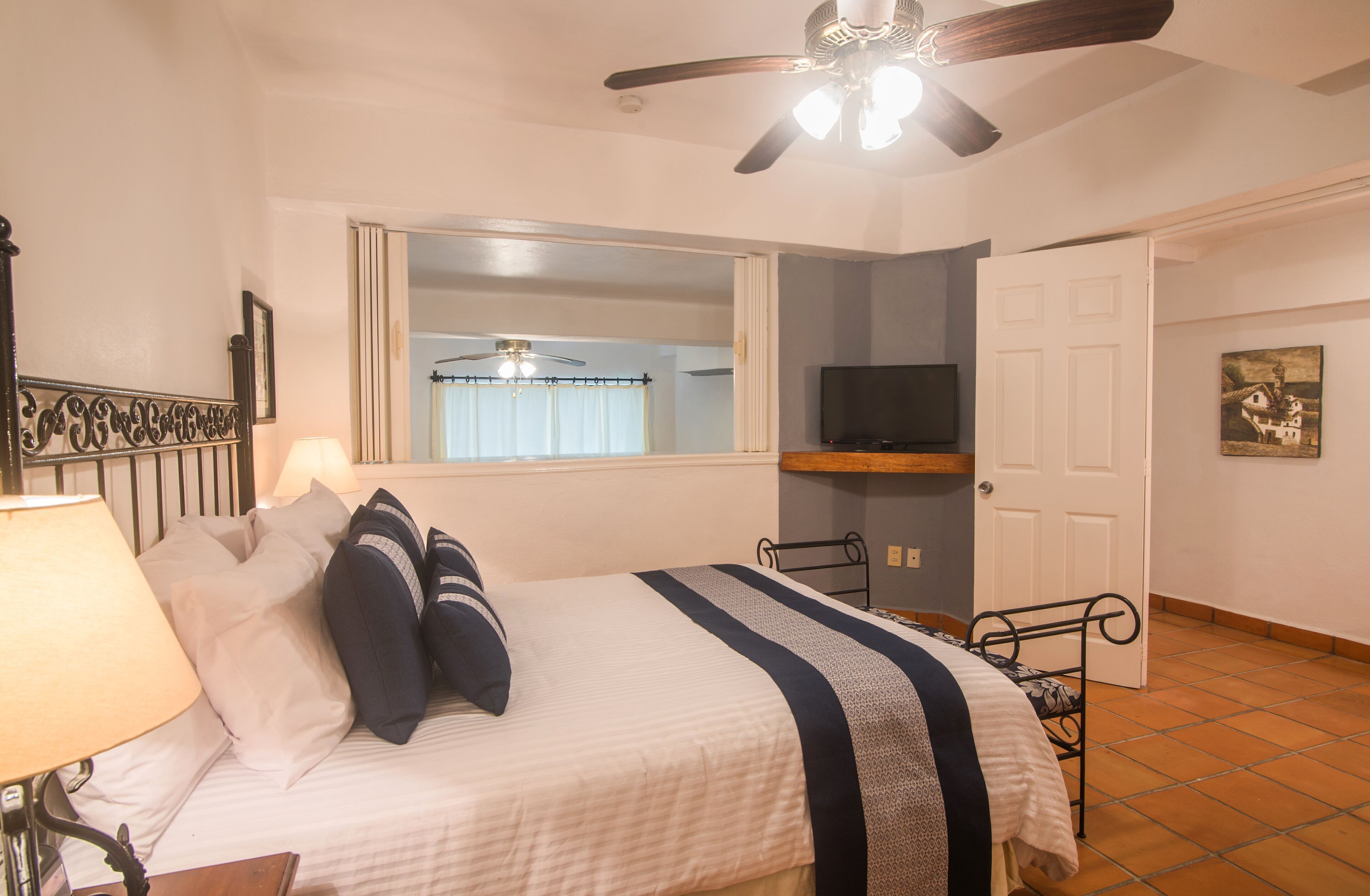 A bedroom with a bed, a ceiling fan, a TV, a window with curtains, and a door.