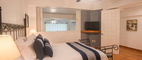 A bedroom with a bed, a ceiling fan, a TV, a window with curtains, and a door.