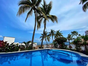 A swimming pool surrounded by palm trees and a clear blue sky. - One Beach Street Puerto Vallarta (Puerto Vallarta)
