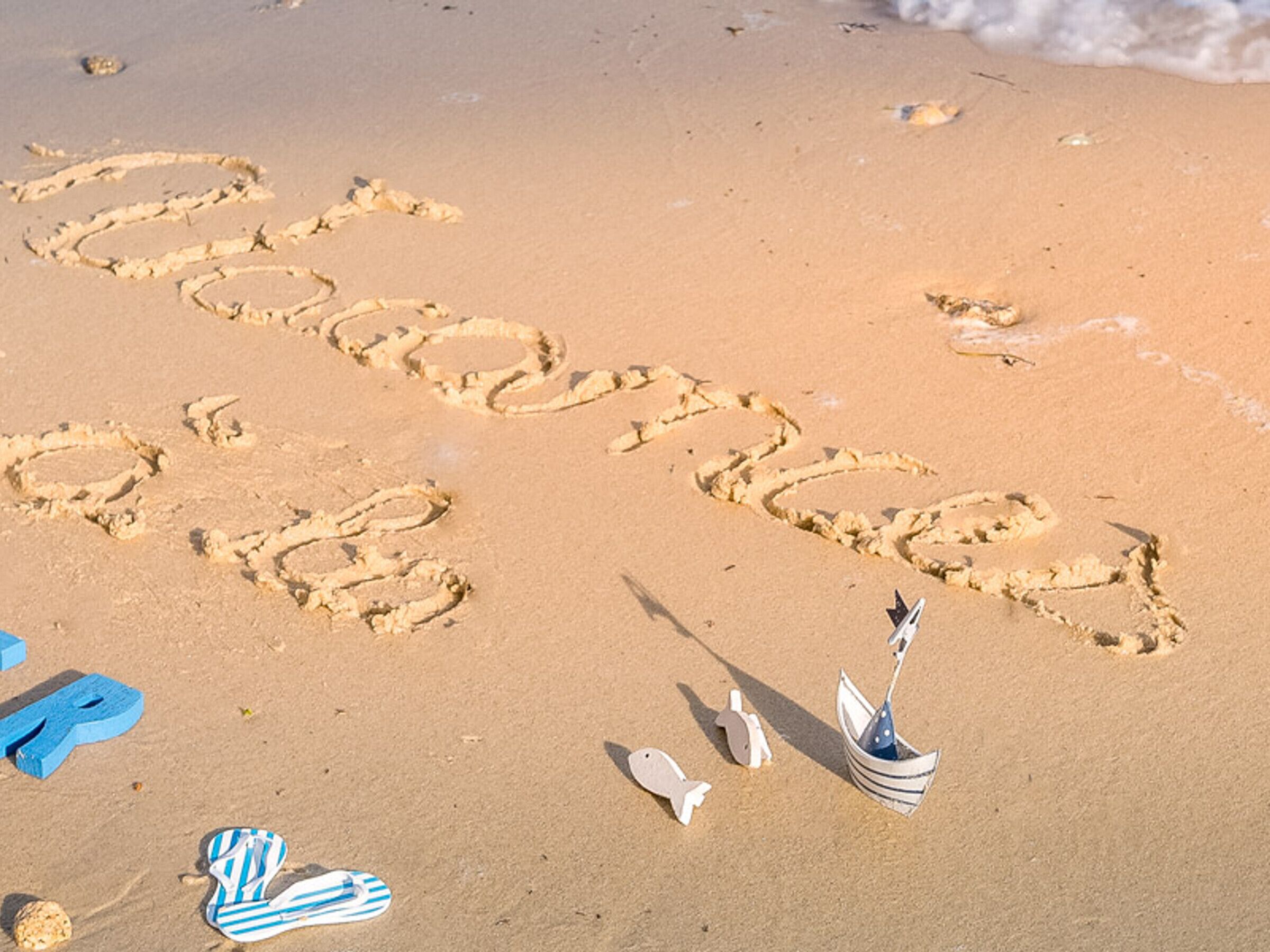 A sandy beach with the word "beach" written in the sand, accompanied by a small boat and a fish.