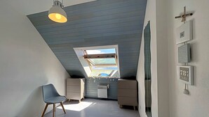 Une chambre avec un plafond en pente, une lucarne, un lit, un bureau et une chaise.