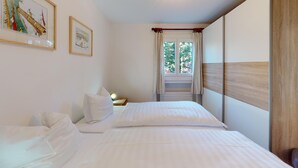 Ein Schlafzimmer mit zwei Betten, einem Fenster mit Vorhängen und gerahmten Kunstwerken an der Wand.