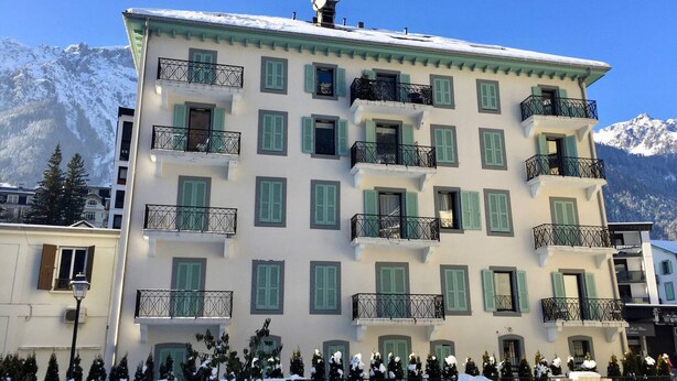 Un edificio de varios pisos con balcones, un paisaje nevado y montañas al fondo.