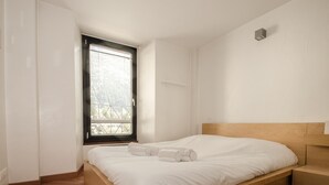Un dormitorio minimalista con cama de madera, un ventanal grande y un banco de madera.