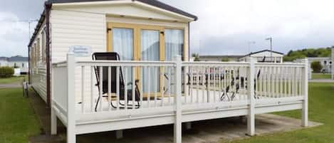 Een stacaravan met een omheind terras, een overdekte zitplek buiten, en een klein bijgebouw.