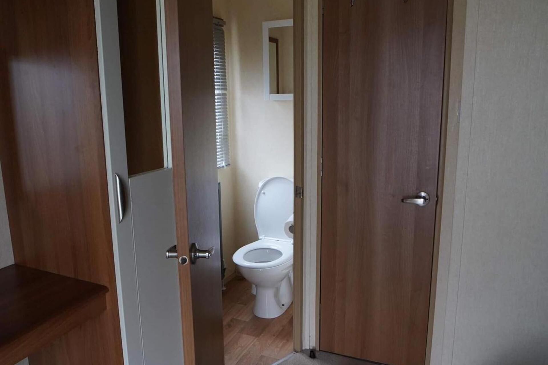 A wooden door leading to a bathroom with a white toilet and a mirror on the wall.