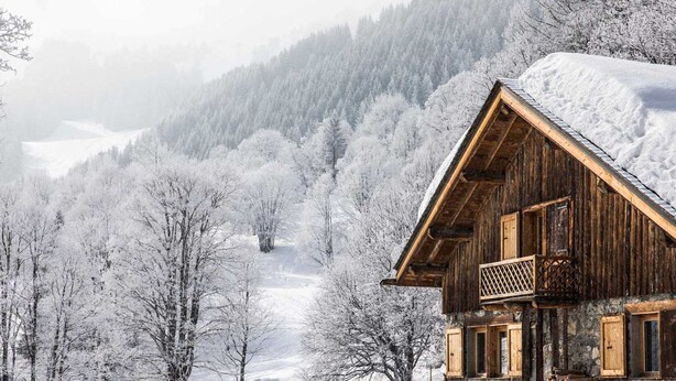 A wooden cabin with a balcony, surrounded by snow-covered trees and a mountainous backdrop. - Spacious chalet in Méribel with sunny terrace and fireplace (Méribel)