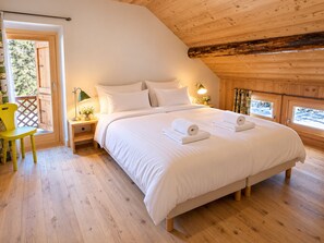 A bedroom with a large bed, wooden flooring, a nightstand with a lamp, and a window with a view. - Spacious chalet in Méribel with sunny terrace and fireplace (Méribel)