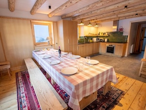 A long dining table set with plates and glasses, wooden benches, a window, a kitchen with a microwave, and a patterned rug. - Spacious chalet in Méribel with sunny terrace and fireplace (Méribel)