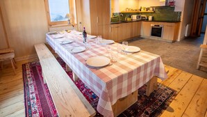 A long dining table set with plates and glasses, wooden benches, a window, a kitchen with a microwave, and a stove. - Spacious chalet in Méribel with sunny terrace and fireplace (Méribel)
