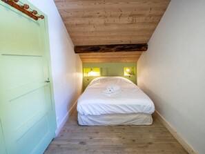 A narrow room with a wooden ceiling, a bed with white bedding, and a green door. - Spacious chalet in Méribel with sunny terrace and fireplace (Méribel)