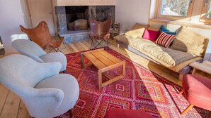 A cozy living room with a stone fireplace, wooden beams, a sofa with cushions, and a patterned rug. - Spacious chalet in Méribel with sunny terrace and fireplace (Méribel)