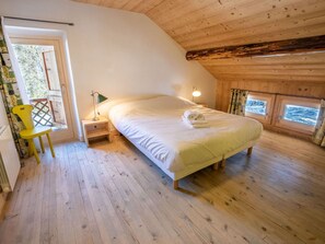 A cozy room with a wooden ceiling, a bed with white linens, a nightstand with a lamp, and a window with a view. - Spacious chalet in Méribel with sunny terrace and fireplace (Méribel)
