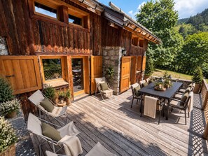 A wooden cabin with a deck, outdoor seating, and a stone wall. - Spacious chalet in Méribel with sunny terrace and fireplace (Méribel)