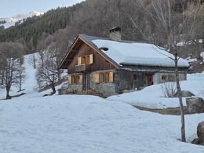 A rustic wooden house with a stone foundation, surrounded by snow-covered landscape and trees. - Spacious chalet in Méribel with sunny terrace and fireplace (Méribel)