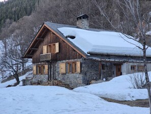 A rustic stone building with a sloped roof and wooden shutters, surrounded by snow. - Spacious chalet in Méribel with sunny terrace and fireplace (Méribel)