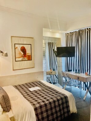 A hotel room with a bed, a desk, a chair, a television, and a framed picture on the wall. - Andromeda Boutique hotel (Kastoria)