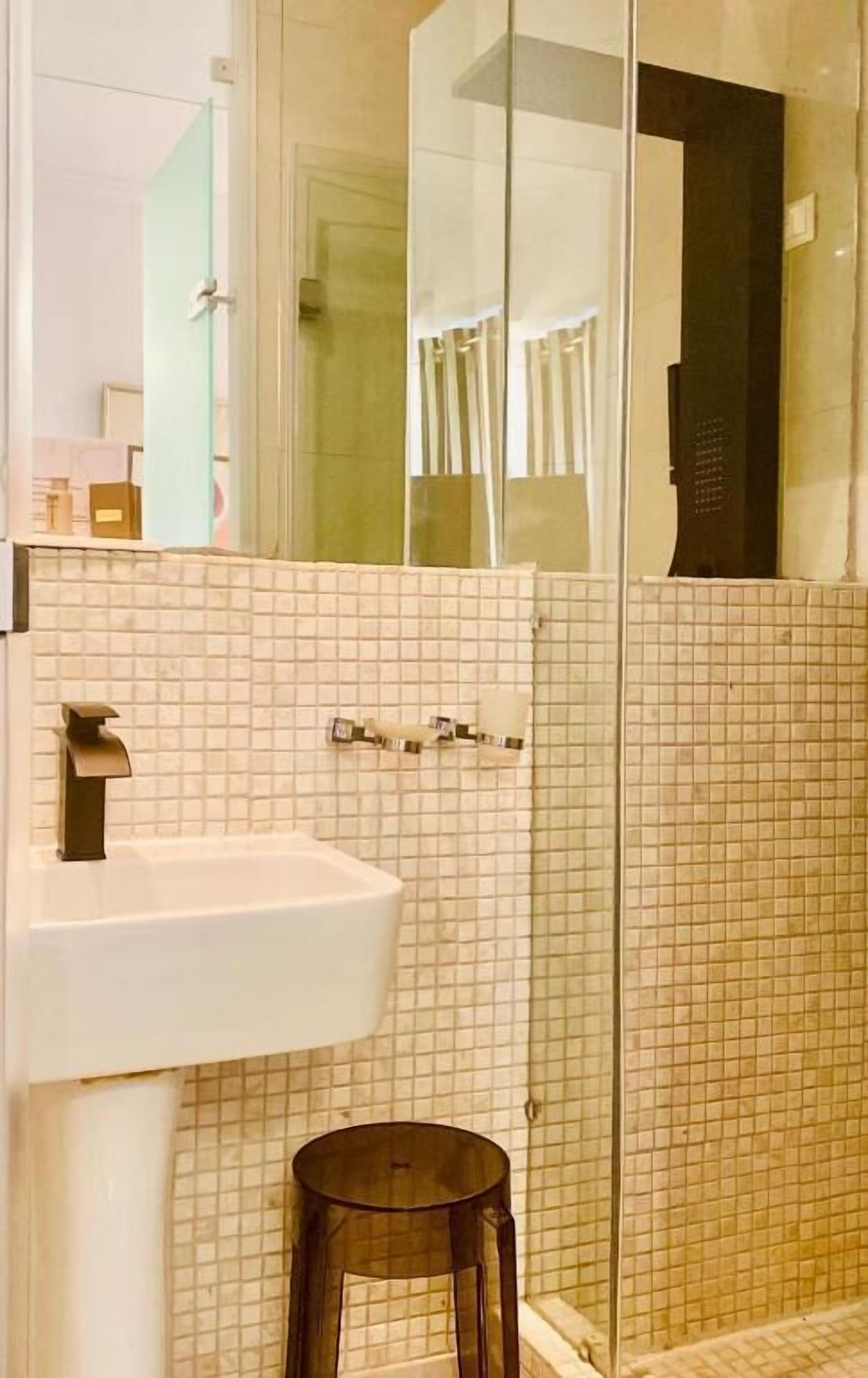 Een badkamer met een wit wastafelmeubel, een douchecabine met glazen wanden en een klein krukje.