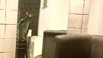 Una habitación con un sofá, una silla, una mesita y un espejo que refleja parte del espacio.