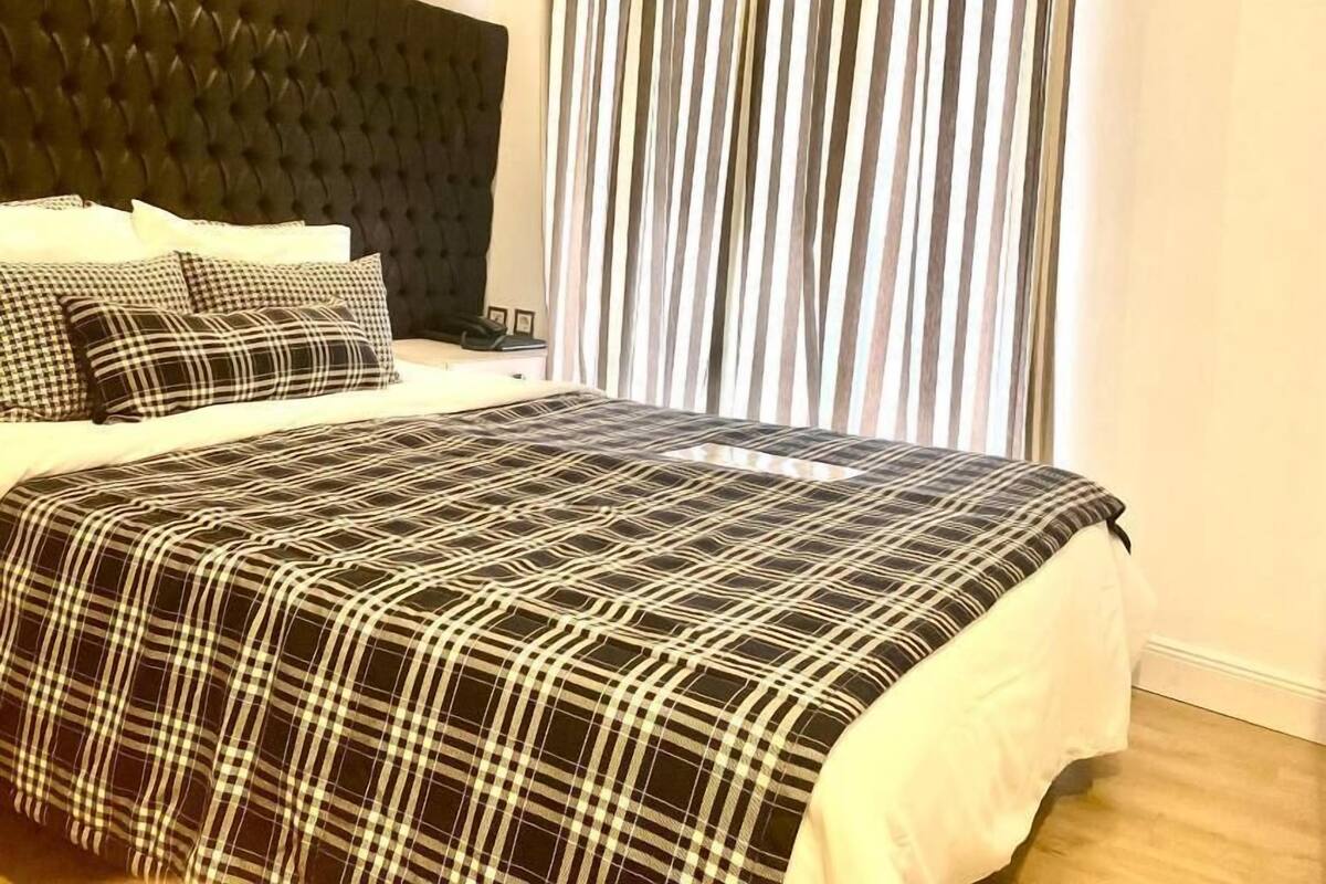 A bedroom with a tufted headboard, a checkered bedspread, and a striped curtain.