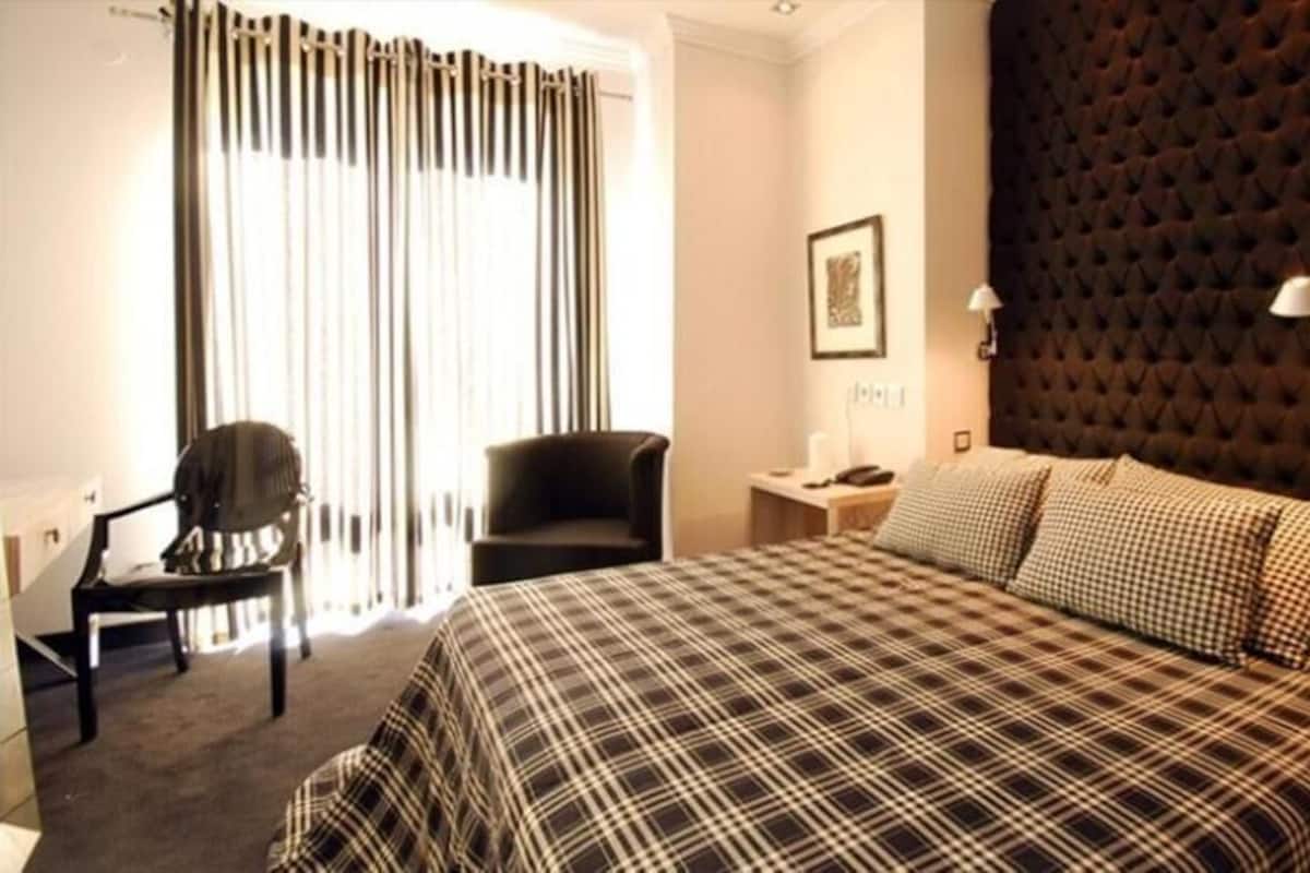 A hotel room with a large bed, a chair, a desk, and a window with curtains.