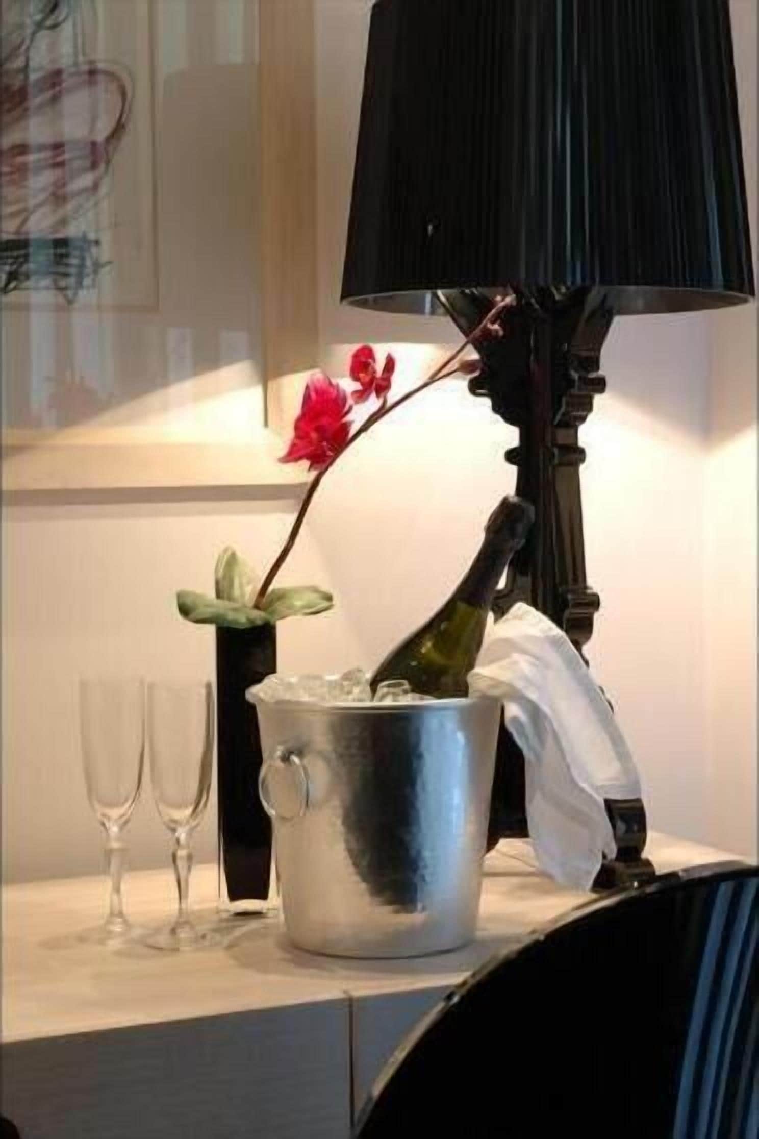 A table with a metal bucket containing a bottle, a vase with a red flower, and two empty wine glasses.