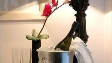 Una mesa con un cubo metálico que contiene una botella, un florero con una flor roja y dos copas de vino vacías.