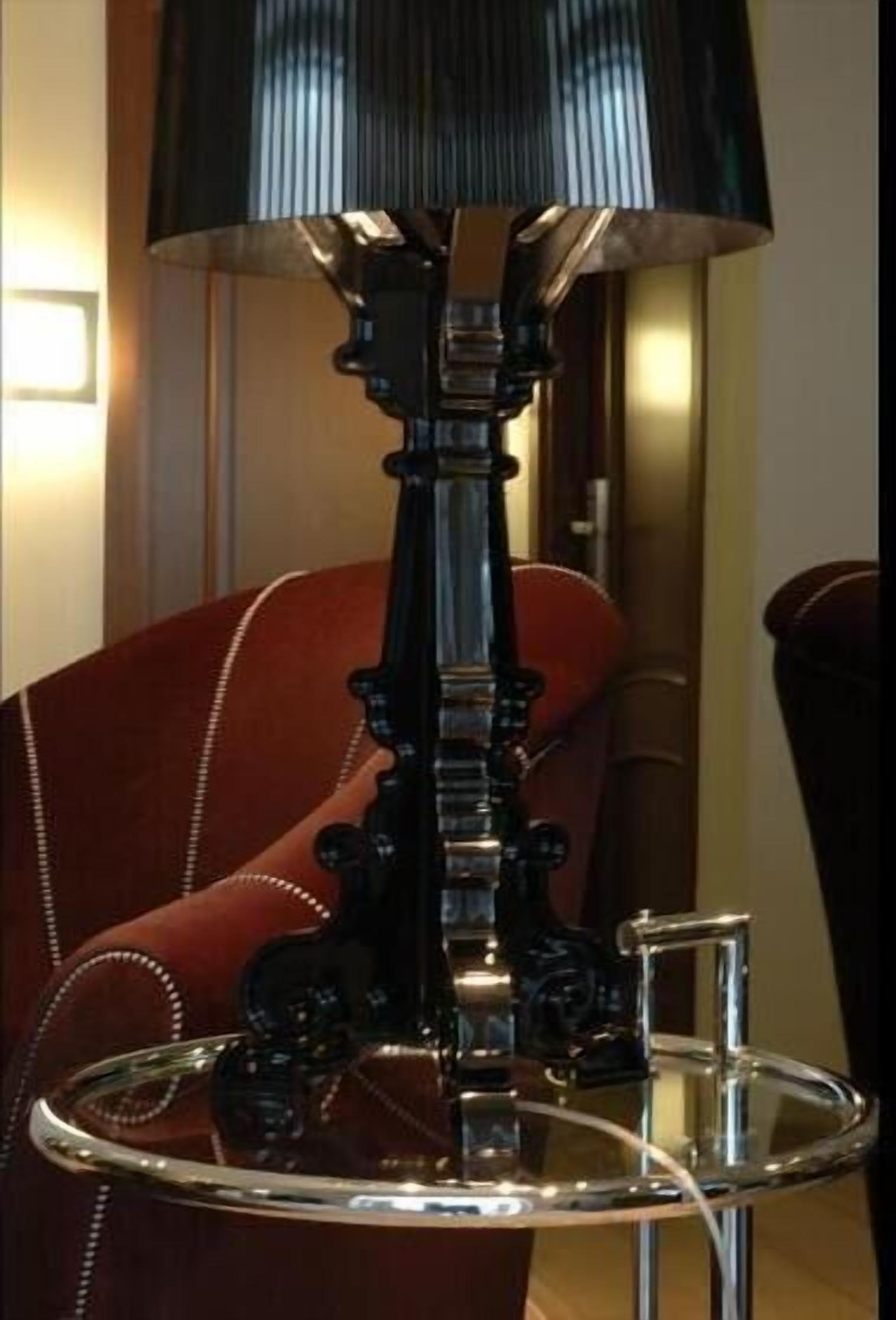 A table lamp with a black shade and a metallic base, placed on a glass table.
