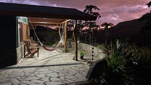 Een terras van natuursteen met een hangmat, tuinmeubels en uitzicht op de bergen.