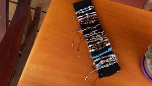 Een tafel met een kleurrijke muurschildering op de achtergrond, een zwarte tas met diverse accessoires, en een houten stoel.