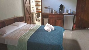 Een slaapkamer met een bed, een klein keukenhoekje en een badkamer die door een open deur zichtbaar is.