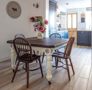 Een eethoek met een houten tafel en stoelen, een vaas met bloemen en een aan de muur bevestigde plaquette.
