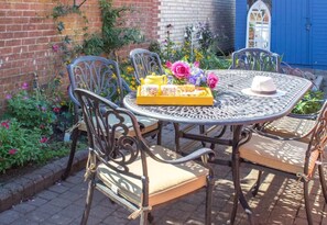 Een ronde metalen tafel met vier stoelen, een dienblad met eten en drinken, en een hoed op tafel.