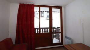 Ein Zimmer mit Holztisch, einem roten Sofa, einem Fenster mit Holzrahmen und Blick auf ein Gebäude.
