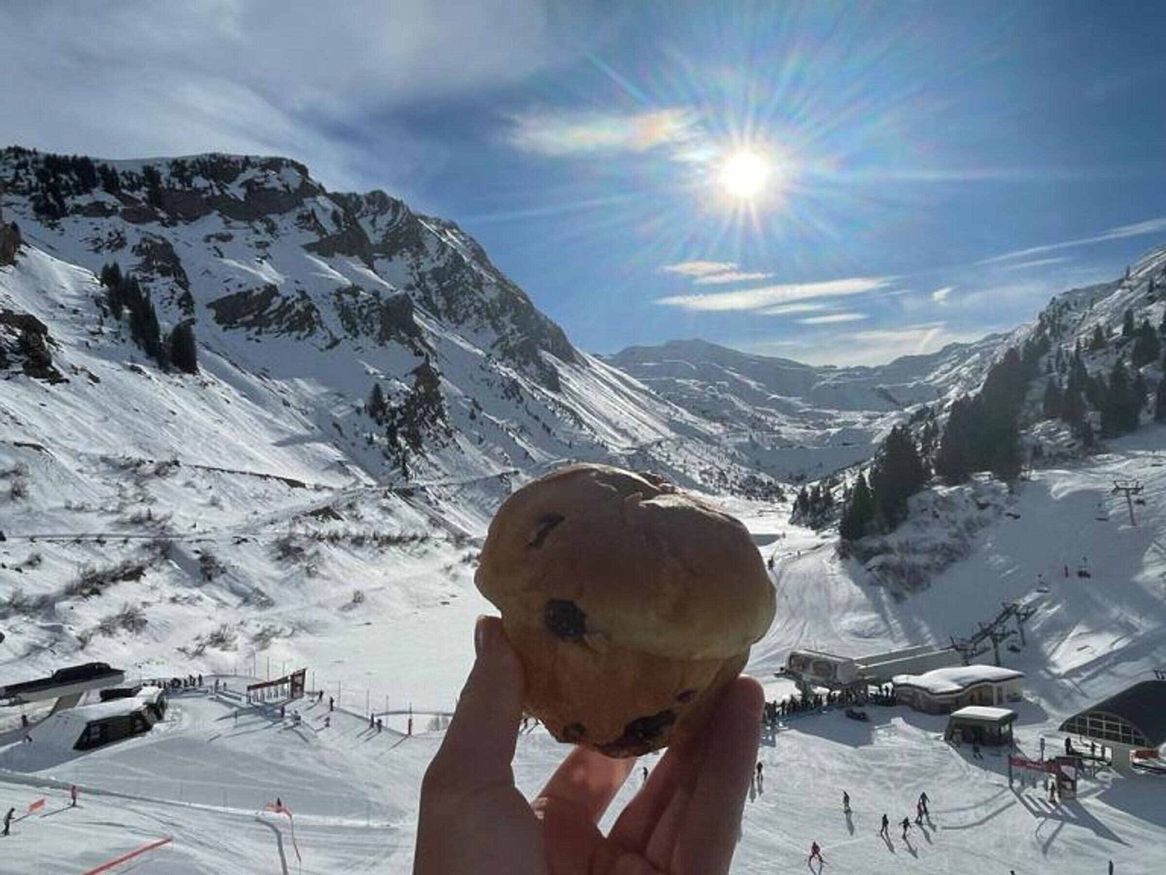 Une main tenant un muffin, avec un paysage de montagne enneigée en arrière-plan.