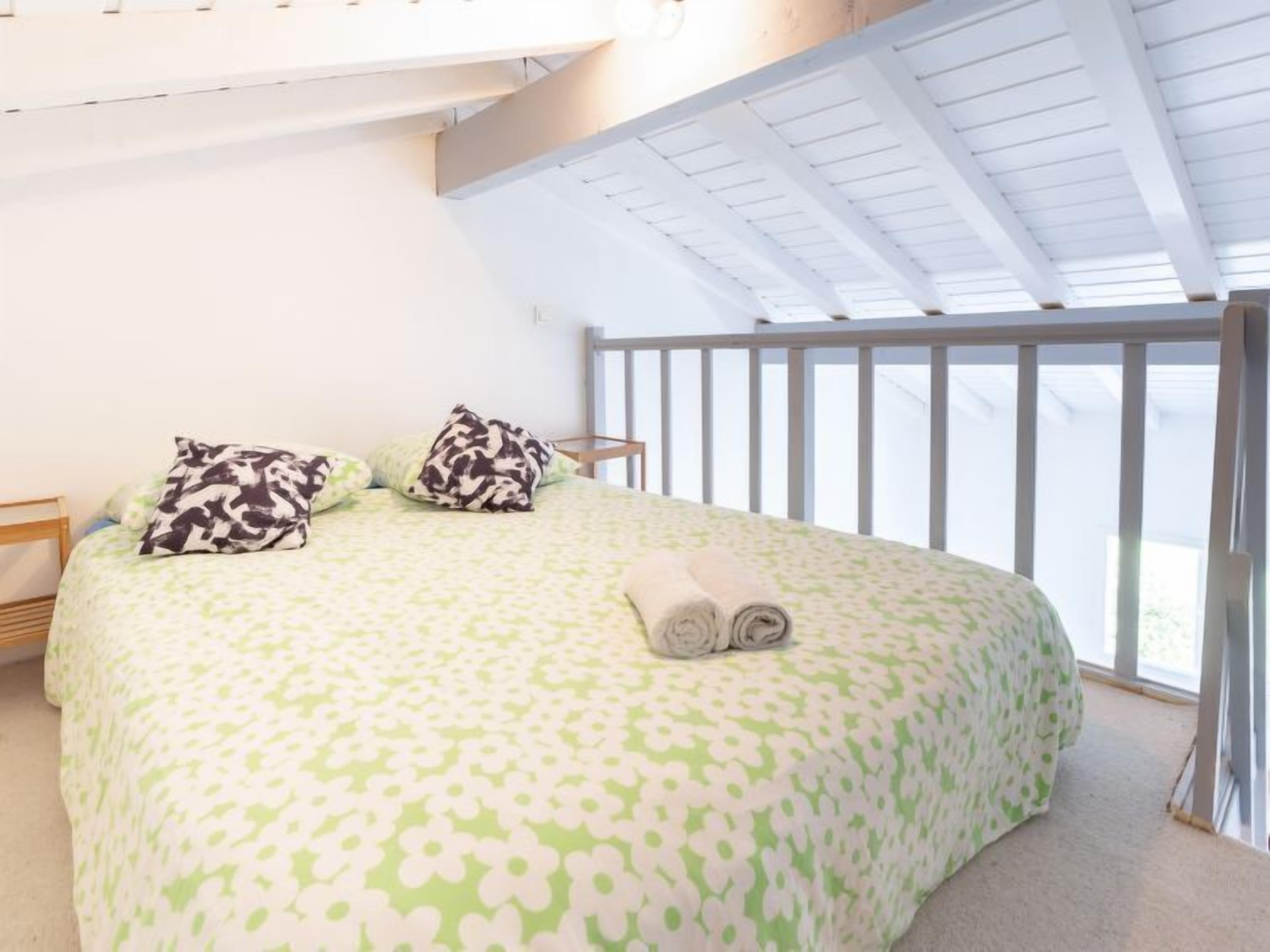 A bedroom with a large bed, two pillows, and a rolled towel.